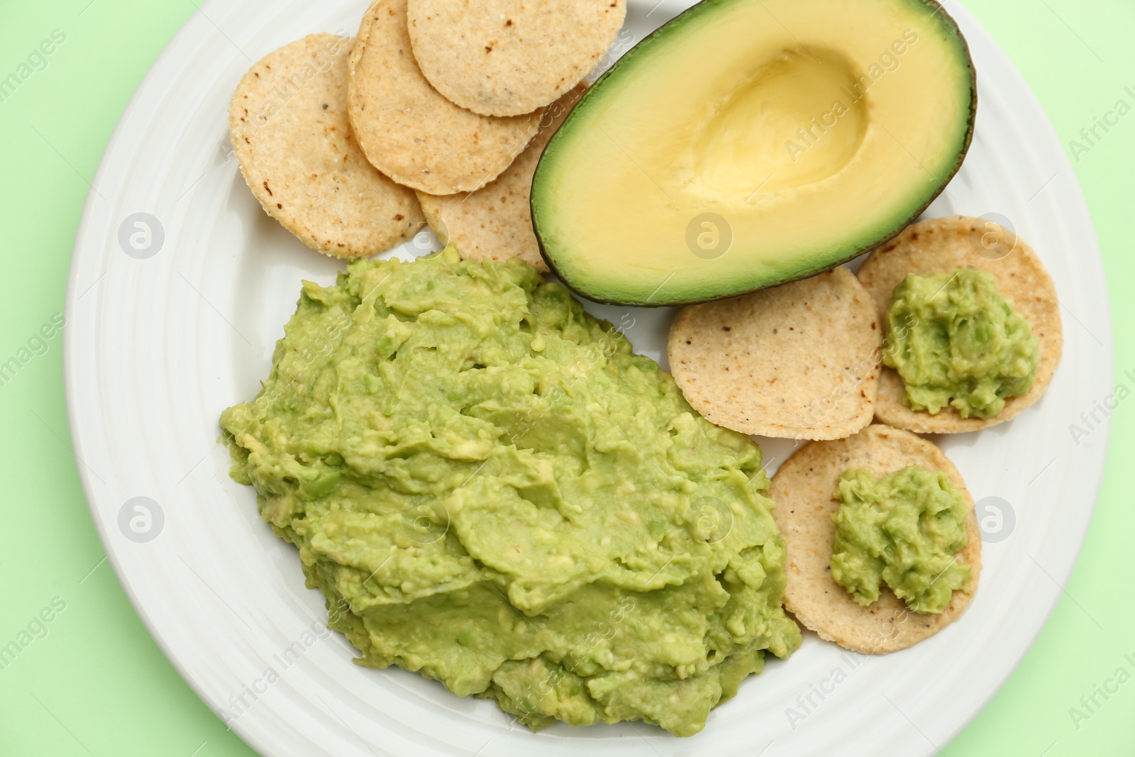 Photo of Delicious guacamole, avocado and chips on light green background, top view