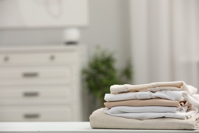 Photo of Stack of different folded clothes on white table indoors, closeup. Space for text