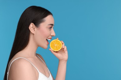 Beautiful young woman with piece of orange on light blue background. Space for text