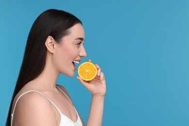 Photo of Beautiful young woman with piece of orange on light blue background. Space for text