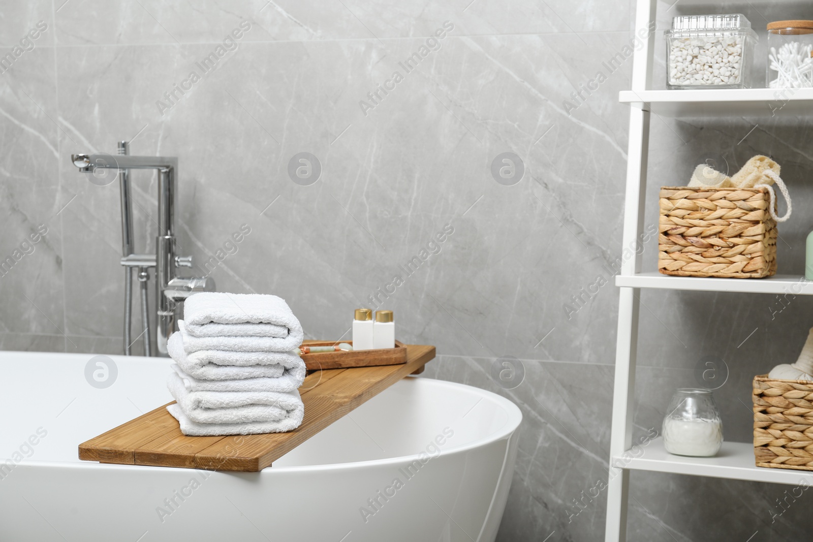 Photo of Stacked bath towels and personal care products on tub tray in bathroom