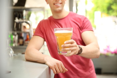 Young man with glass of cold beer near bar counter