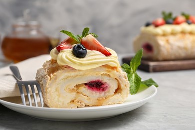 Photo of Piece of tasty meringue roll with jam, cream, strawberry, blueberry and mint on light grey table, closeup
