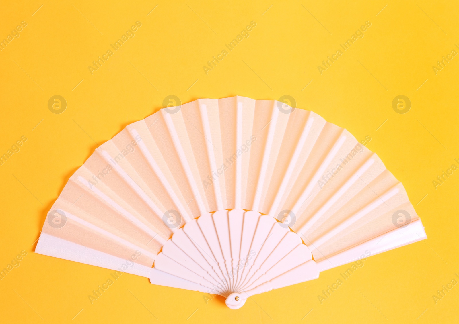 Photo of White hand fan on yellow background, top view