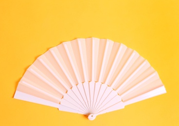 White hand fan on yellow background, top view