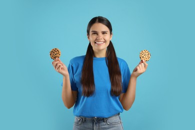 Photo of Young woman with chocolate chip cookies on light blue background