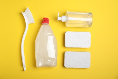 Photo of Cleaning supplies for dish washing on yellow background, flat lay