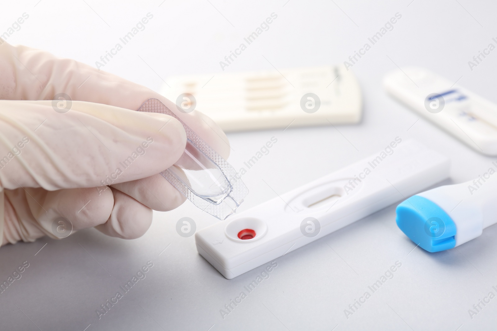 Photo of Doctor dropping buffer solution onto disposable express test cassette on light background, closeup