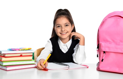 Photo of Little girl in uniform doing assignment at desk against white background. School stationery