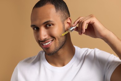 Handsome man applying cosmetic serum onto face on light brown background
