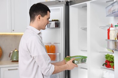 Man putting container with vegetables into refrigerator in kitchen