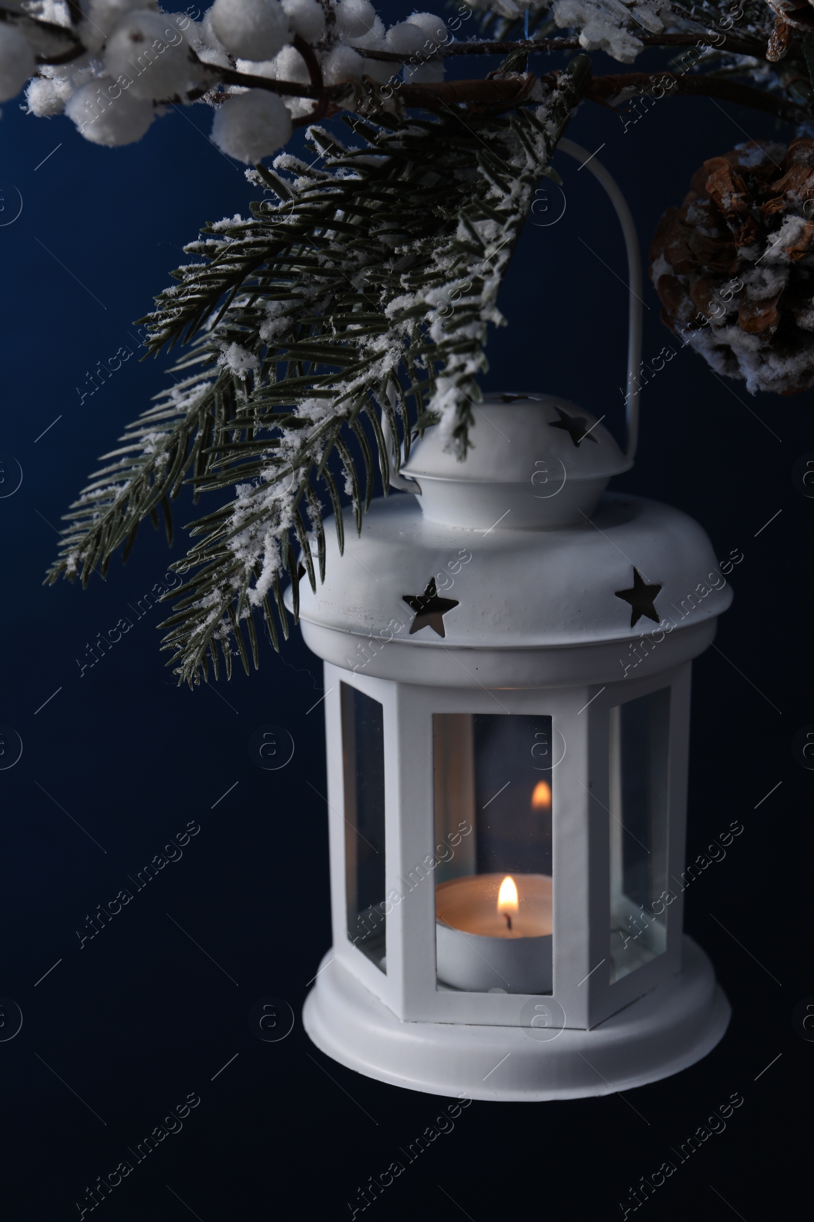 Photo of Christmas lantern with burning candle on fir tree against blue background. closeup