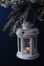 Photo of Christmas lantern with burning candle on fir tree against blue background. closeup