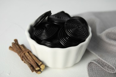 Photo of Tasty black candies and dried sticks of liquorice root on white table, closeup