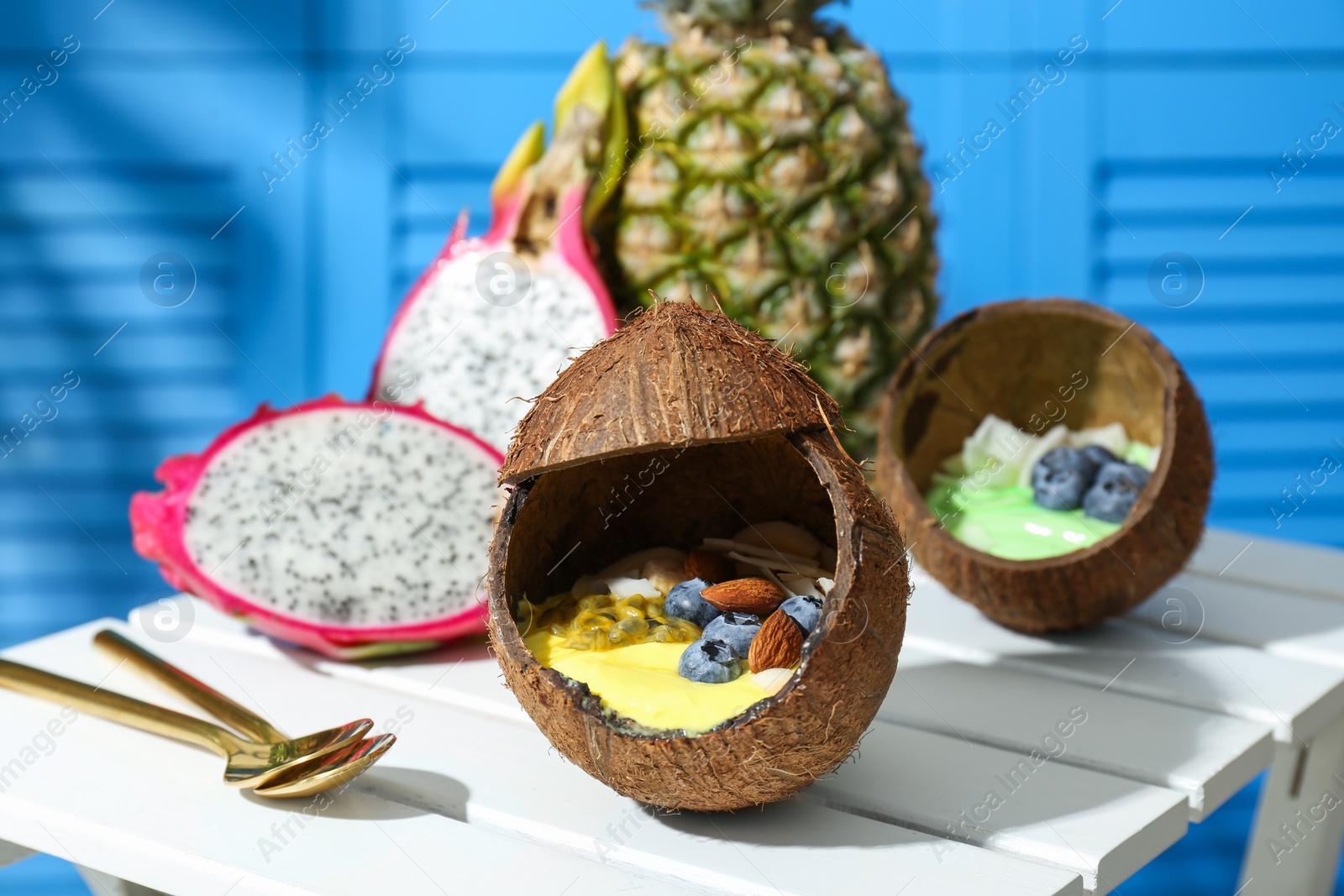 Photo of Tasty smoothie bowl served in coconut shells on white wooden table