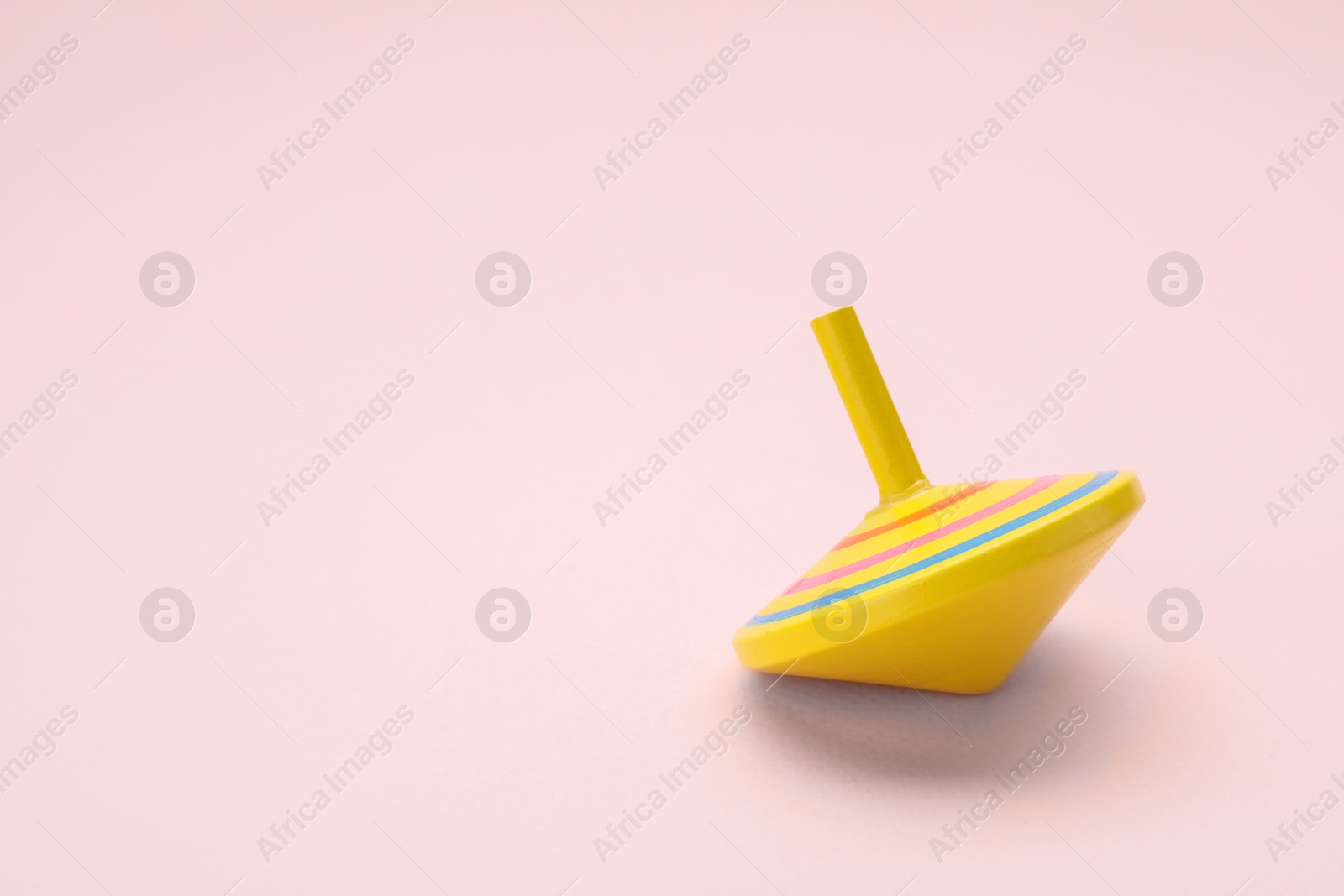 Photo of One bright spinning top on beige background, space for text. Toy whirligig