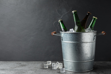 Photo of Metal bucket with beer and ice cubes on grey background. Space for text