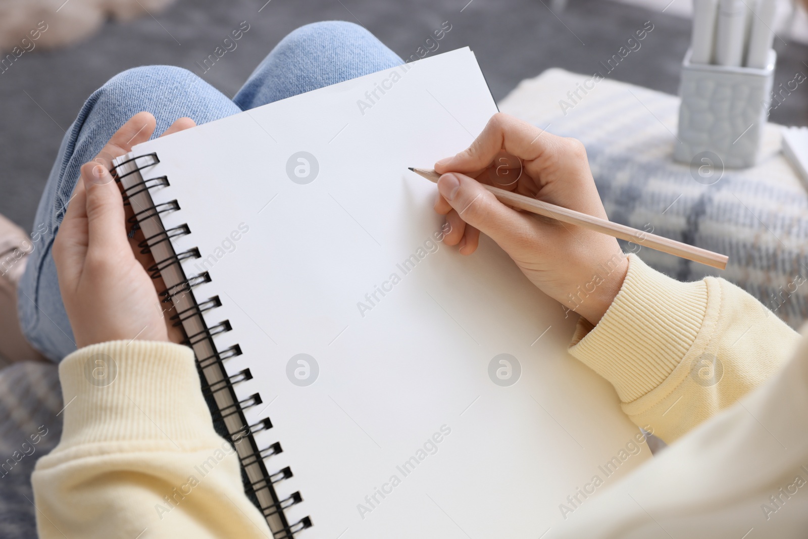 Photo of Young woman drawing in sketchbook indoors, closeup