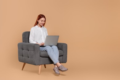 Photo of Smiling young woman working with laptop in armchair against beige background, space for text