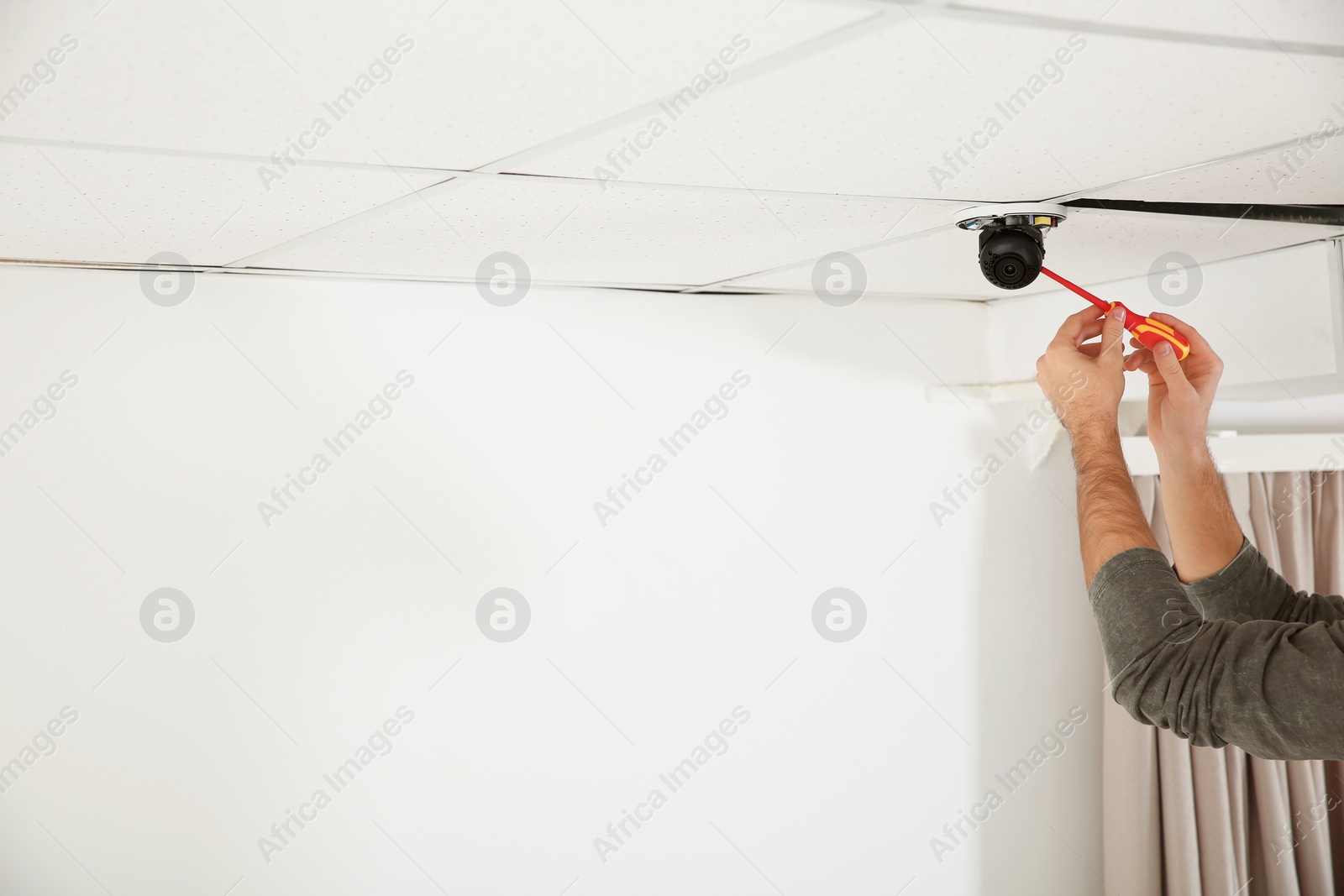 Photo of Electrician with screwdriver repairing CCTV camera indoors, closeup. Space for text