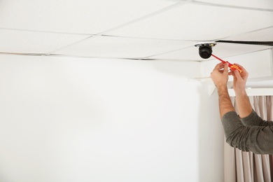 Electrician with screwdriver repairing CCTV camera indoors, closeup. Space for text