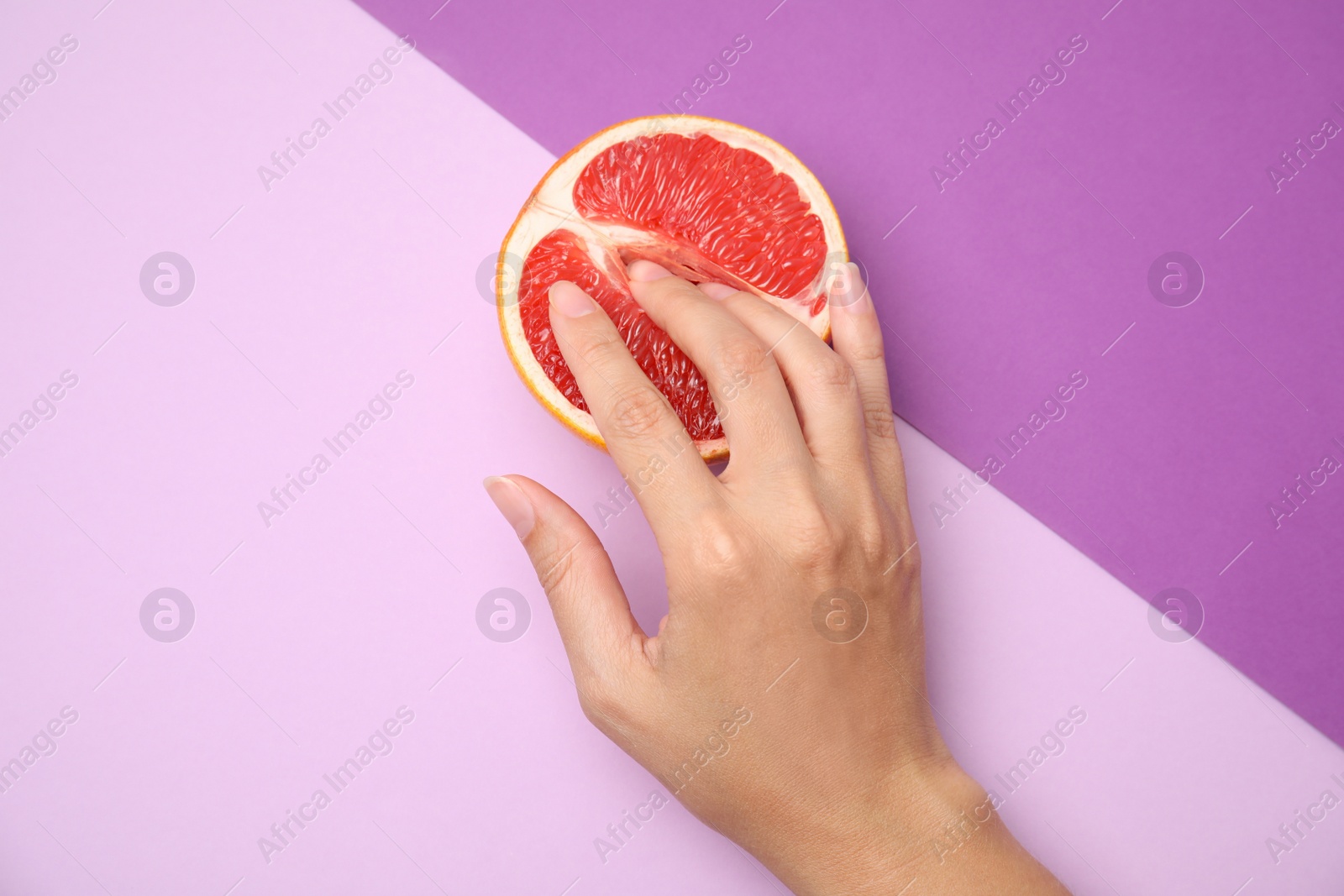 Photo of Young woman touching half of grapefruit on color background, above view. Sex concept