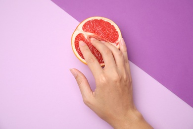 Photo of Young woman touching half of grapefruit on color background, above view. Sex concept