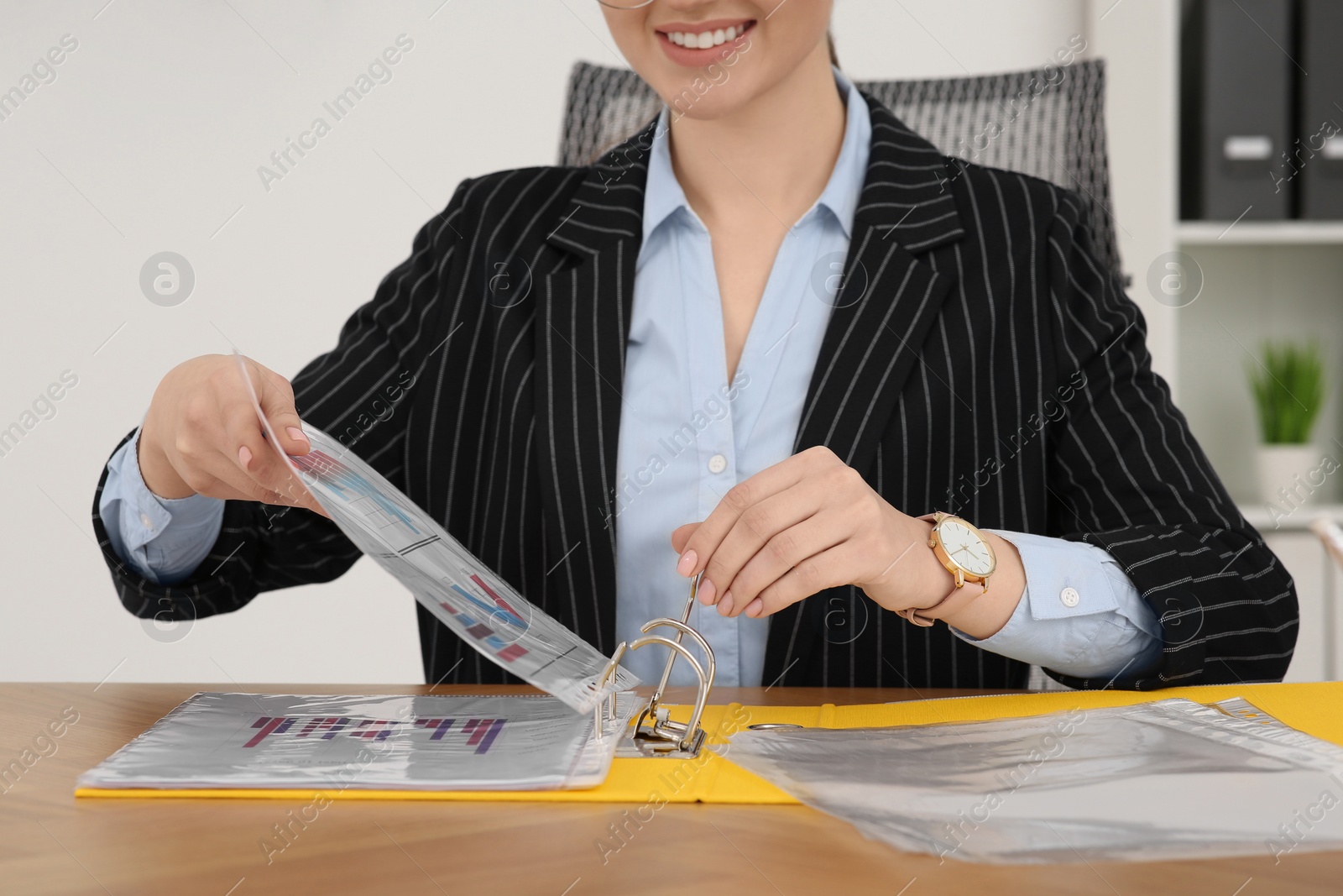 Photo of Businesswoman putting document into file folder at wooden table in office, closeup