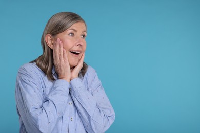 Portrait of surprised senior woman on light blue background, space for text