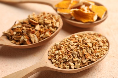 Photo of Spoons with dried orange seasoning zest and peel on beige textured table, closeup