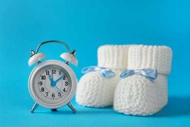 Alarm clock and baby booties on light blue background. Time to give birth