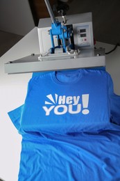 Photo of Printing logo. Heat press with blue t-shirt on white table
