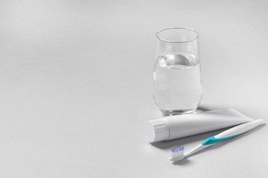 Photo of Plastic toothbrush with paste and glass of water on grey background, space for text