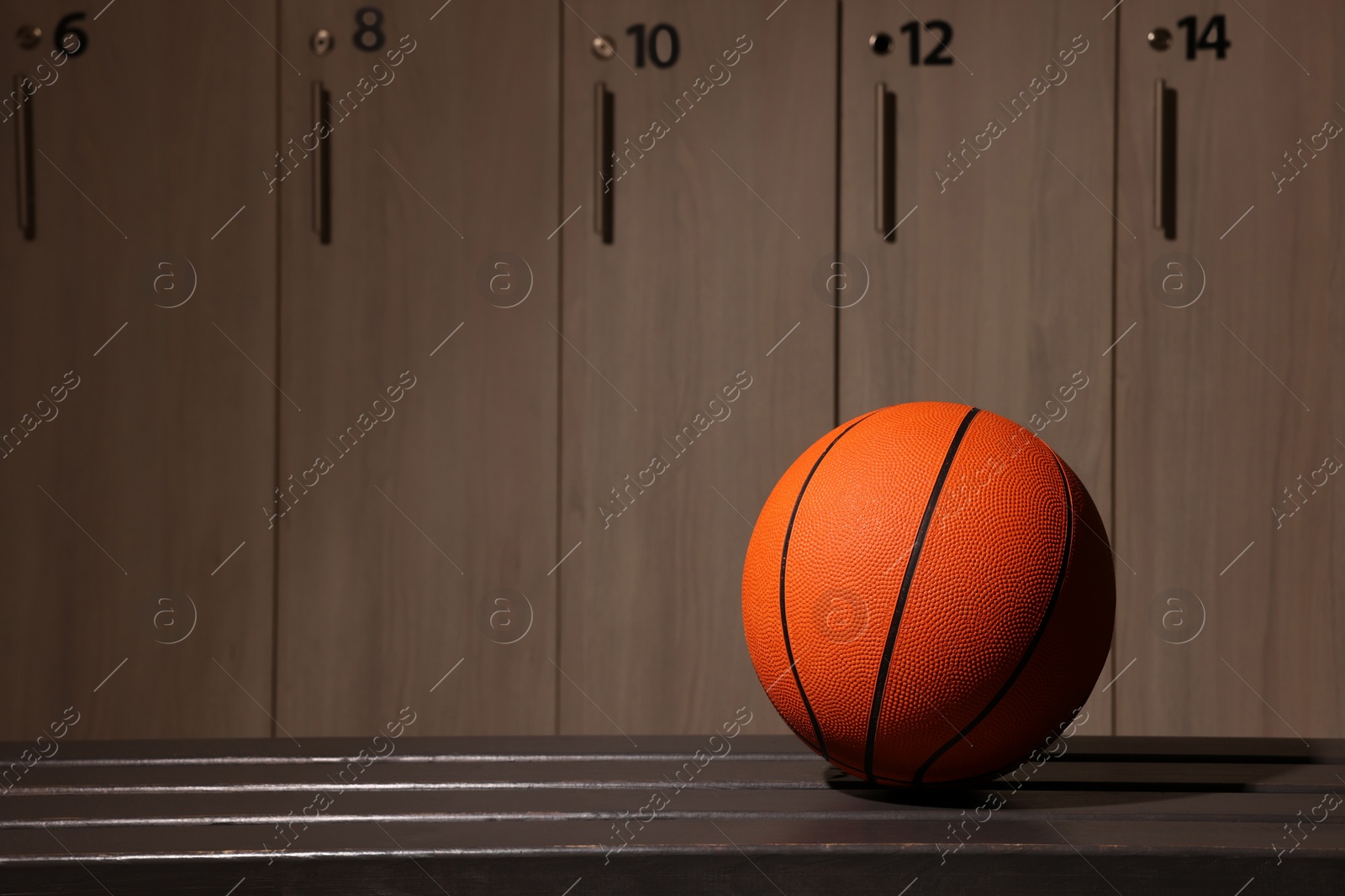 Photo of Orange basketball ball on wooden bench in locker room. Space for text