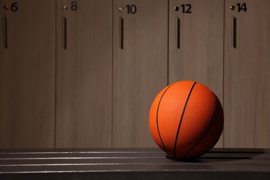 Orange basketball ball on wooden bench in locker room. Space for text