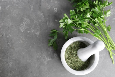 Photo of Mortar with dry parsley and space for text on grey table, top view