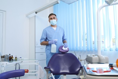 Photo of Professional dentist in uniform cleaning workplace  with antiseptic indoors