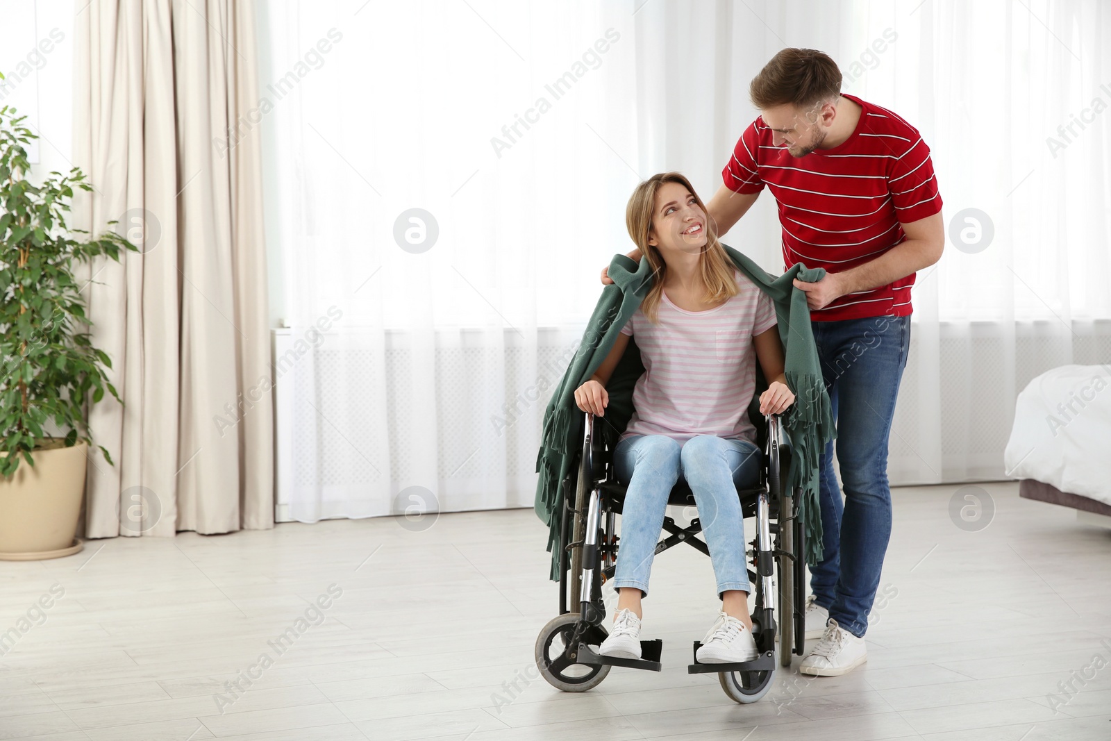 Photo of Man covering woman in wheelchair with plaid at home. Helping disabled