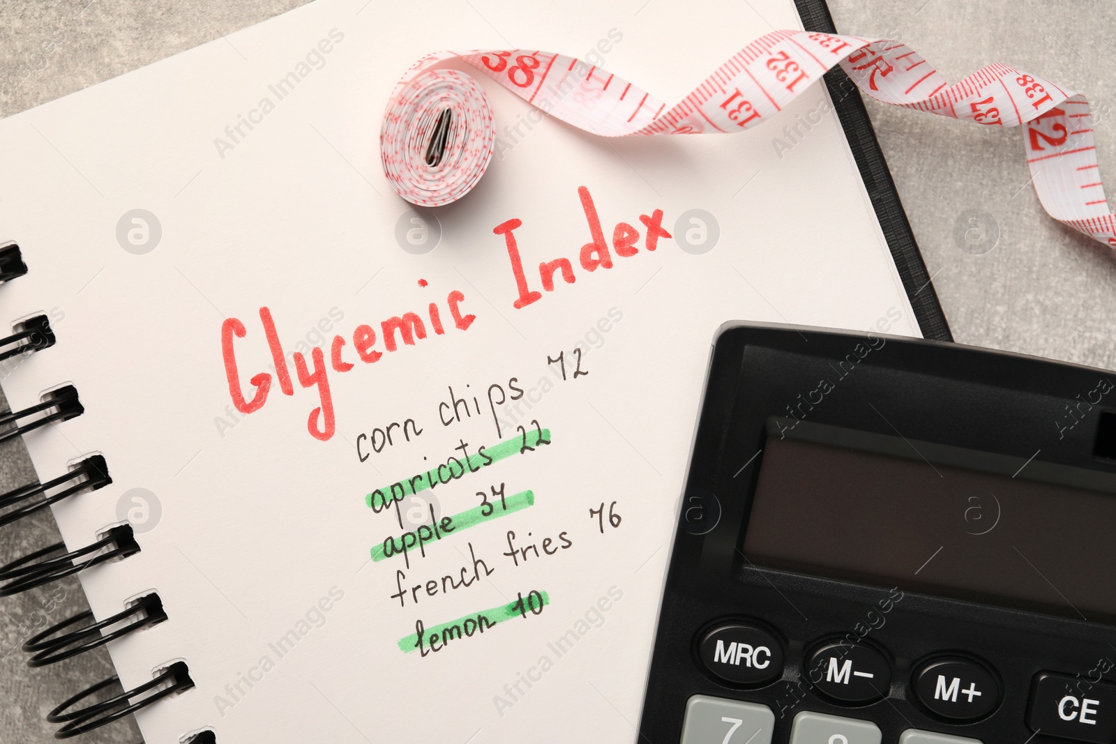 Photo of Glycemic Index. Notebook with information, measuring tape and calculator on light grey table, flat lay
