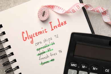 Photo of Glycemic Index. Notebook with information, measuring tape and calculator on light grey table, flat lay