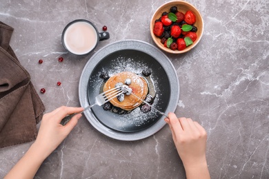 Woman eating delicious pancakes with berries and powdered sugar at table