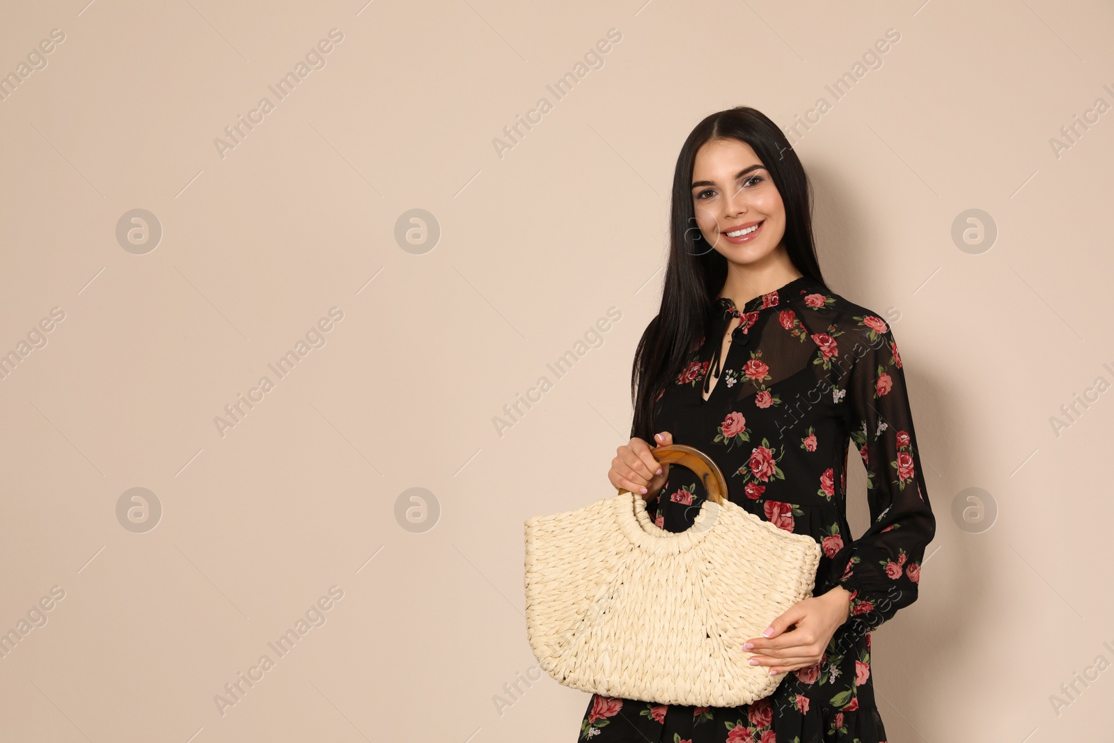 Photo of Young woman wearing floral print dress with straw bag on beige background. Space for text