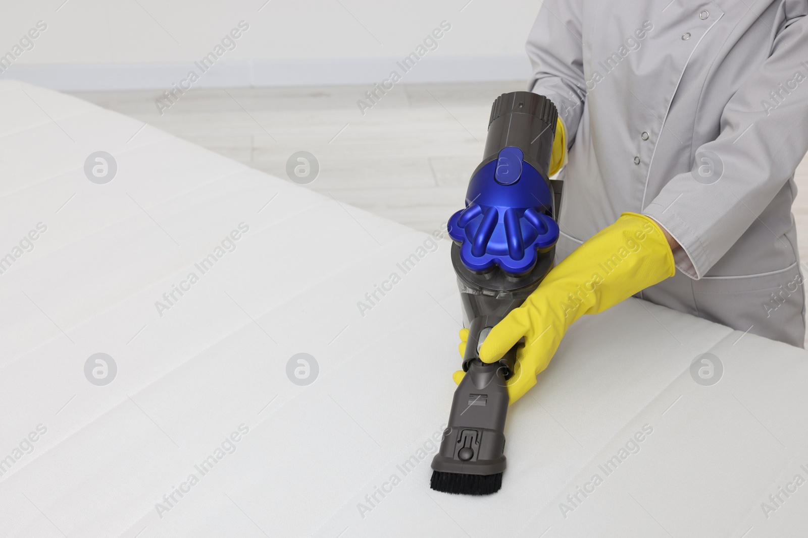 Photo of Woman in gloves disinfecting mattress with vacuum cleaner indoors, closeup. Space for text