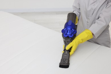 Photo of Woman in gloves disinfecting mattress with vacuum cleaner indoors, closeup. Space for text