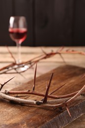 Photo of Crown of thorns and glass with wine on wooden table, selective focus