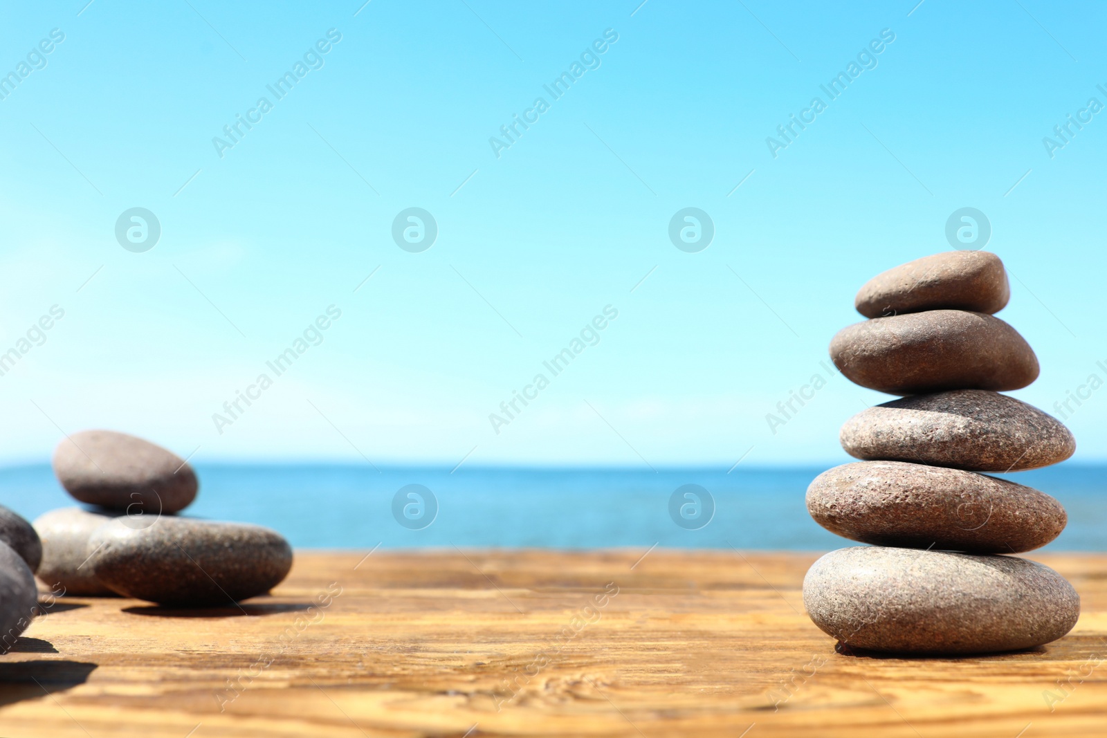 Photo of Stack of stones on wooden table against seascape, space for text. Zen concept