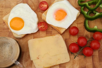 Photo of Tasty toasts with fried eggs, cheese and vegetables on wooden board, flat lay