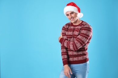 Photo of Portrait of young man in Christmas sweater and Santa hat on light blue background. Space for text