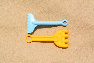 Colorful plastic rakes on sand, flat lay. Beach toys