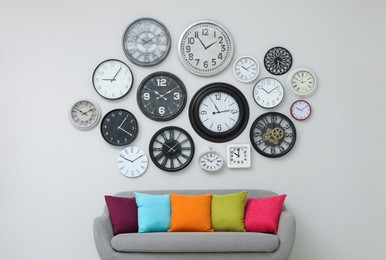 Sofa and many different clocks hanging on white wall in room